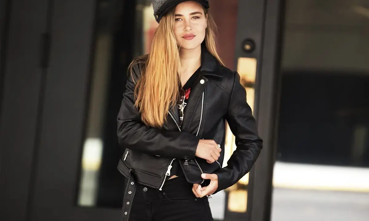 Dziewczyna w czarnej ramonesce i czapce, z długimi blond włosami, emanuje rockowym, glam rock stylem.
