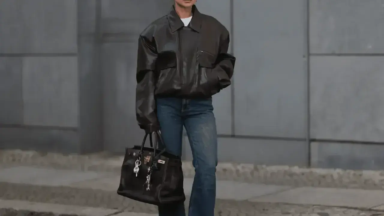 Kobieta w brązowej, oversize'owej kurtce i jeansach, z torbą w ręku. Stylizacja nawiązuje do punk rocka, z luźnymi elementami i mocnym akcentem.