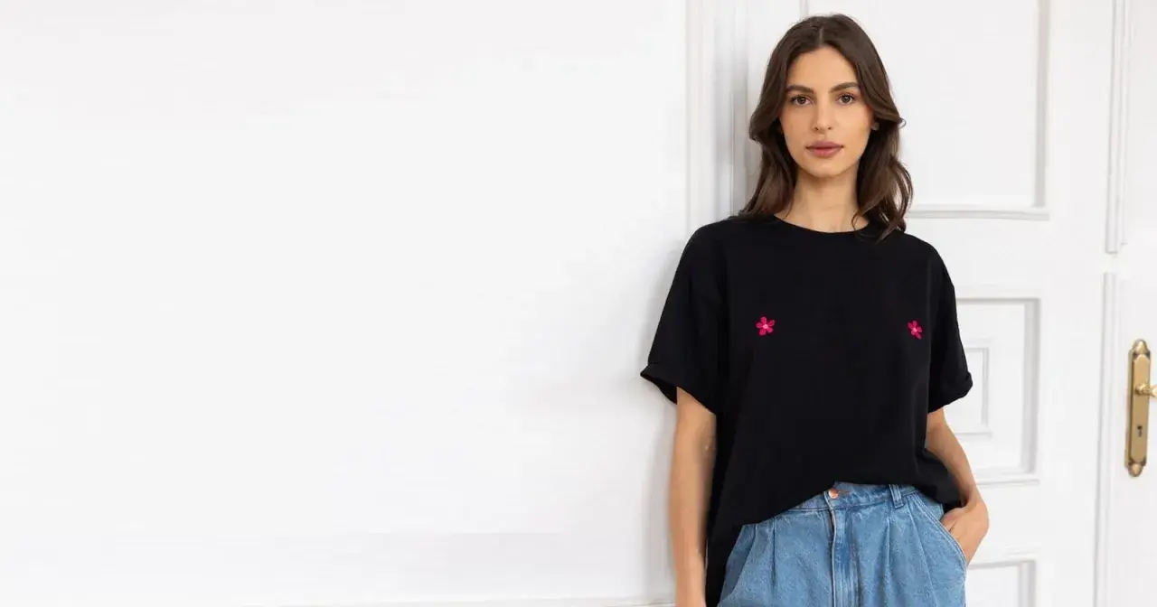 Kobieta w czarnym t-shircie z haftowanymi kwiatkami i jeansach. Stylowy sposób, jak nosić t-shirt w spodniach.