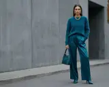 Kobieta w eleganckim, futrzanym swetrze i satynowych spodniach w kolorze petrol. Torebka i buty również w tym samym odcieniu.