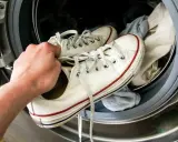 Białe trampki z czerwonymi i niebieskimi paskami, wyciągane z pralki, z widocznymi zaciekami na butach po praniu.