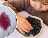 Małe rączki sięgają po jagody, zostawiając na białym materiale charakterystyczne plamy z jagód.