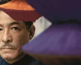 Portret mężczyzny z wąsikiem, otoczonego przez japońskich projektantów mody, w barwnych, geometrycznych formach.