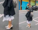 Elegancka koronkowa spódnica stylizacje z czarną marynarką i siatkową torbą. Kobieta w okularach przeciwsłonecznych i szarej bluzce z długim rękawem.