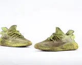 Para zielonych adidas Yeezy 350 z charakterystyczną, prążkowaną podeszwą, gotowe na miejskie przygody.