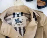 Beżowy trencz Burberry z charakterystycznym wzorem w kratę i herbem.
