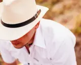 Mężczyzna w białej koszuli i słomkowym kapeluszu z czarną opaską, uosobienie stylu country męskiego.