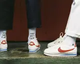 Stare modele butów Nike Cortez w klasycznej odsłonie. Białe z czerwonym logo i niebieskim paskiem. Na skarpetkach napis "YOUR LIFE IS A JOKE".