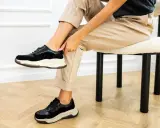 Kobieta w beżowych spodniach i czarnych sneakersach. Dowiedz się, jak szybko wysuszyć buty po praniu, by znów cieszyć się komfortem.