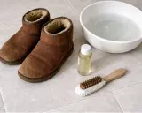 Brązowe buty UGG, miska z wodą, buteleczka z płynem i szczotka do czyszczenia. Dowiedz się, jak czyścić UGG.