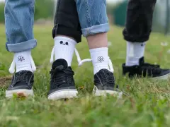 Białe skarpety na spodniach z zabawnymi buźkami i ramionami, noszone z czarnymi trampkami na trawie.