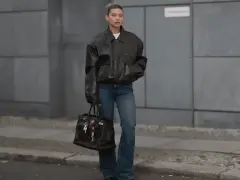 Kobieta w brązowej, oversize'owej kurtce i jeansach, z torbą w ręku. Stylizacja nawiązuje do punk rocka, z luźnymi elementami i mocnym akcentem.
