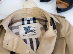 Beżowy trencz Burberry z charakterystycznym wzorem w kratę i herbem.