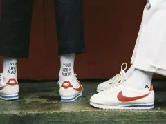 Stare modele butów Nike Cortez w klasycznej odsłonie. Białe z czerwonym logo i niebieskim paskiem. Na skarpetkach napis "YOUR LIFE IS A JOKE".