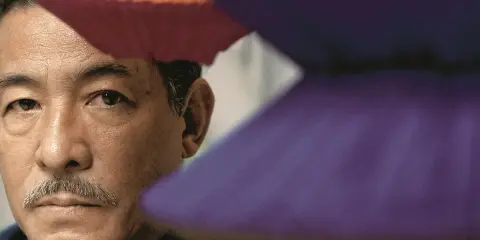 Portret mężczyzny z wąsikiem, otoczonego przez japońskich projektantów mody, w barwnych, geometrycznych formach.