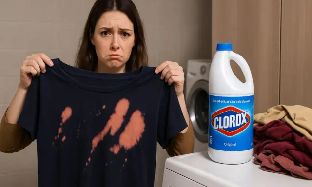 Smutna kobieta pokazuje ciemną koszulkę z pomarańczowymi plamami po wybielaczu. Obok butelka wybielacza Clorox i stos ubrań.