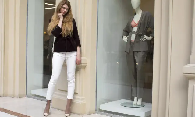 Modelka w białych spodniach i bordowej marynarce obok manekina w eleganckim stroju. Skandynawskie marki odzieżowe prezentują najnowsze trendy.