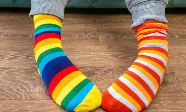Kolorowe skarpetki w paski, tęczowe i pomarańczowo-białe, leżą na drewnianej podłodze. Jak doprać kolorowe skarpetki?
