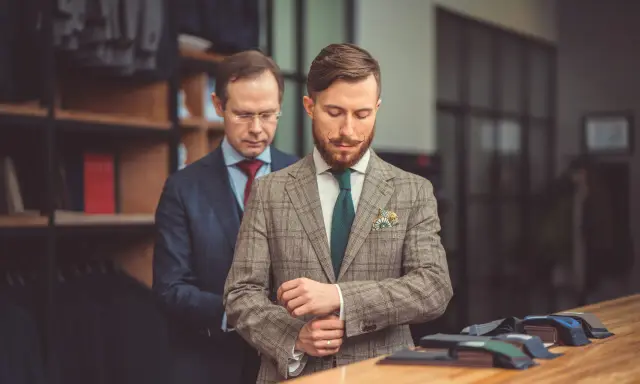 Mężczyzna w garniturze Hugo Boss poprawia mankiet w butiku. Różnica między Hugo a Hugo Boss jest subtelna, ale widoczna w jakości.