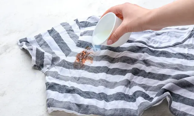 Jak usunąć plamy z czekolady? Płynny środek wylewany na brudny, pasiasty t-shirt.