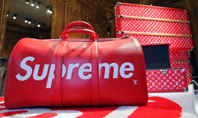 Czerwona torba podróżna z białym logo Supreme. Supreme to marka znana z limitowanych kolekcji i kolaboracji, jak ta z Louis Vuitton.