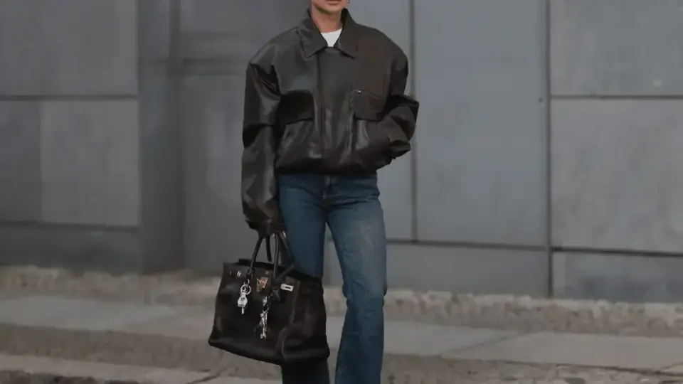 Kobieta w brązowej, oversize'owej kurtce i jeansach, z torbą w ręku. Stylizacja nawiązuje do punk rocka, z luźnymi elementami i mocnym akcentem.