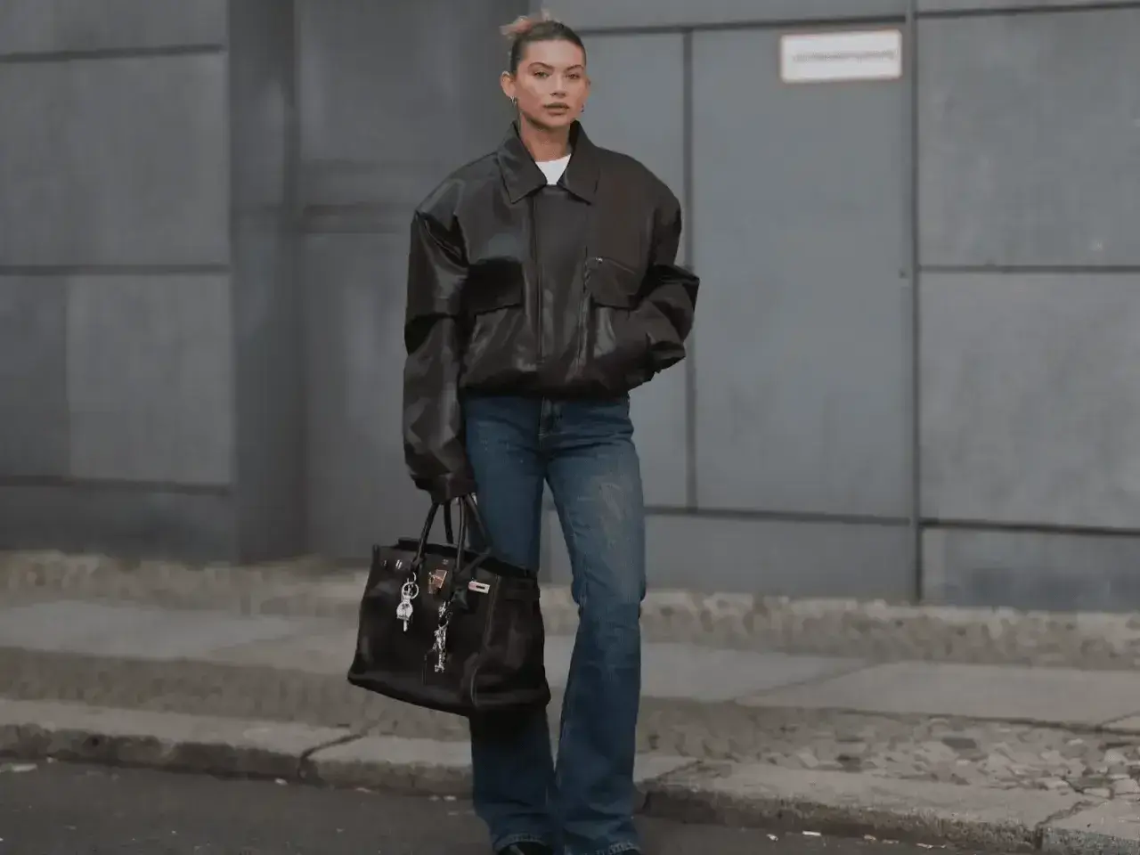 Kobieta w brązowej, oversize'owej kurtce i jeansach, z torbą w ręku. Stylizacja nawiązuje do punk rocka, z luźnymi elementami i mocnym akcentem.