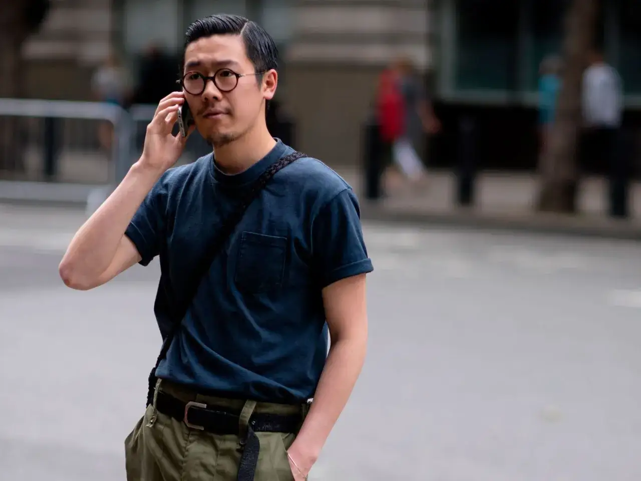 Mężczyzna w okularach rozmawia przez telefon, nosząc granatowy t-shirt wpuszczony w zielone spodnie. Stylowy sposób, jak nosić t-shirt w spodniach.