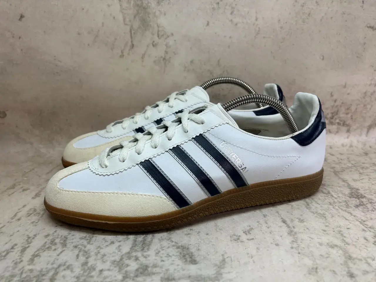 Białe sneakersy Adidas Universal z granatowymi paskami i zamszowym noskiem, klasyczne modele butów adidas z lat 90.