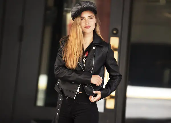 Dziewczyna w czarnej ramonesce i czapce, z długimi blond włosami, emanuje rockowym, glam rock stylem.