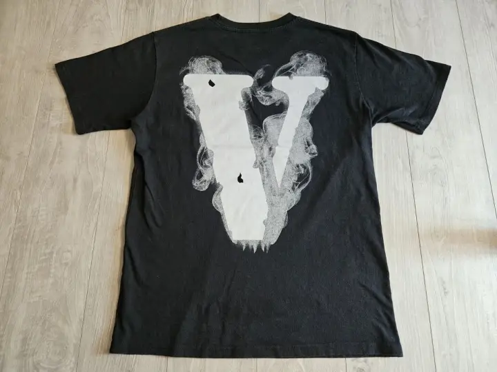 Czarna koszulka z białym, dymiącym logo V. Zastanawiasz się, vlone co to? To właśnie ten styl.