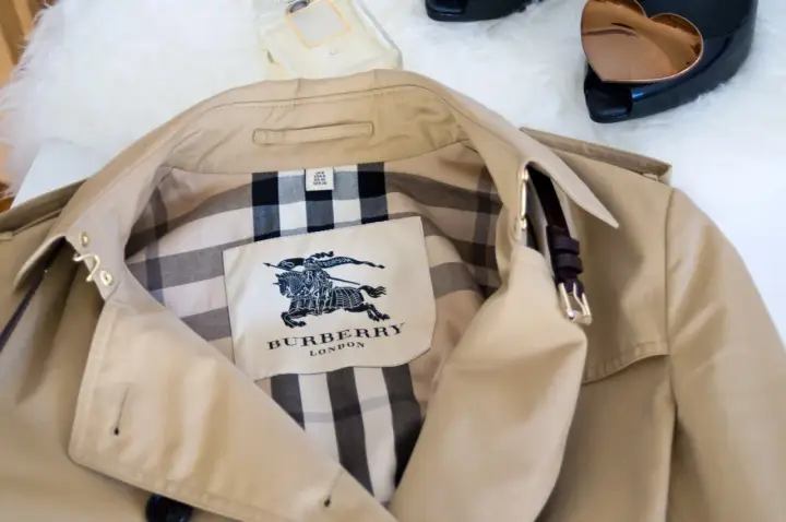 Beżowy trencz Burberry z charakterystycznym wzorem w kratę i herbem.