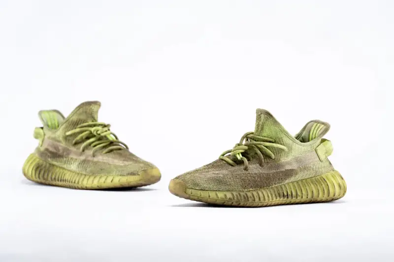 Para zielonych adidas Yeezy 350 z charakterystyczną, prążkowaną podeszwą, gotowe na miejskie przygody.
